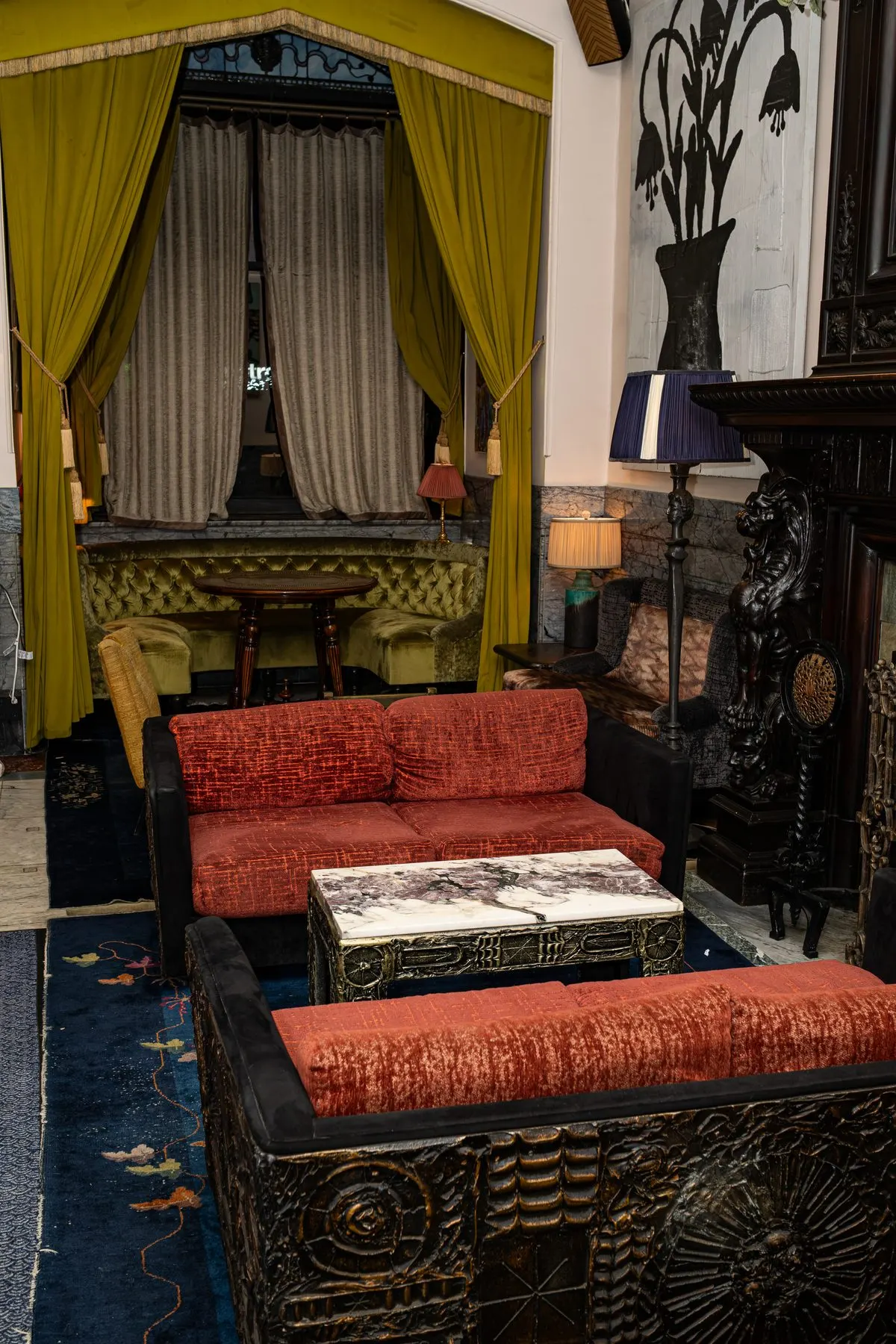 A lounge corner: yellow curtains, red velvet banquettes, a marble table