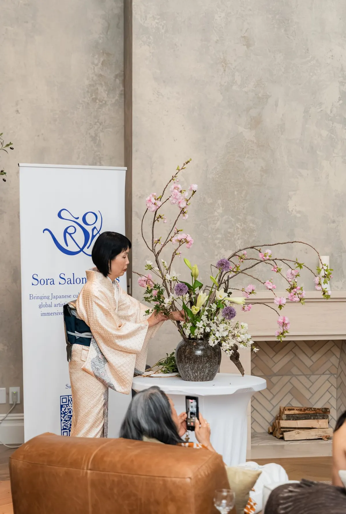 The ikebana artist arranging cherry blossom and lilies by the banner